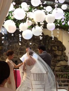the bride and groom are getting married in front of hanging paper lanterns on the ceiling
