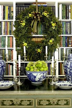 a table topped with blue and white bowls filled with green apples next to bookshelves