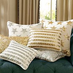 gold and white pillows on a green couch in front of a window with drapes