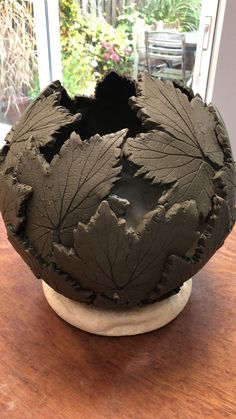 a clay vase sitting on top of a wooden table next to a planter filled with leaves