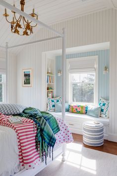 a white bed sitting under a window next to a chandelier in a bedroom
