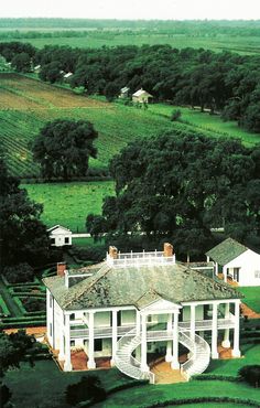 an aerial view of a large white house in the middle of a lush green field