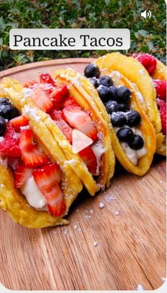 pancakes with strawberries and blueberries are on a cutting board next to some bushes