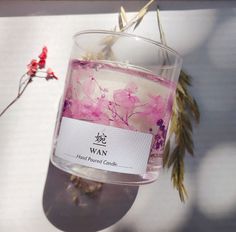 a candle with pink flowers in it sitting on a table next to some dried plants