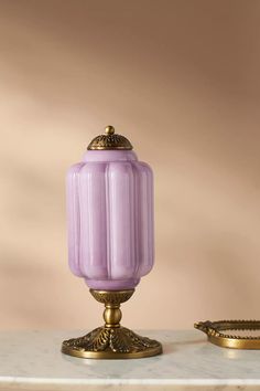 a purple glass candle sitting on top of a table next to a gold plated object