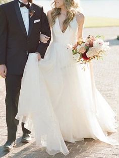a bride and groom holding hands walking down the street in front of water with their bouquets