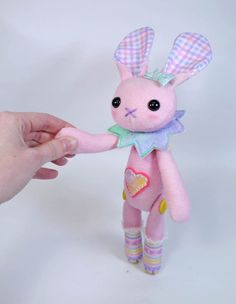 a pink stuffed animal with a checkered shirt and leggings is being held by a person's hand