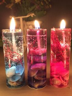 three candles are lit in glass containers filled with sand and shells