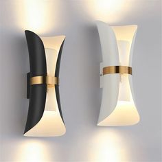 two modern wall lights mounted to the side of a white wall with gold trimmings