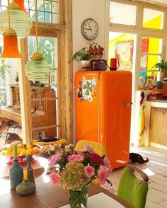 an orange refrigerator sitting inside of a kitchen next to a table with flowers in it