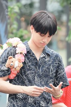 a young man is holding a teddy bear and flowers in his hand while looking down at his cell phone