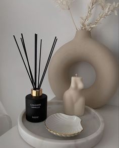 a white vase sitting on top of a table next to a black and white candle