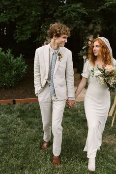 a bride and groom holding hands walking through the grass with flowers in their bouquets