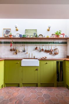 a kitchen with green cabinets and tile flooring is pictured in this image, there are pots on the shelves above the sink