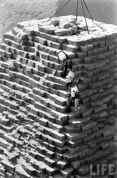 an old black and white photo of two people on top of a brick structure with water in the background
