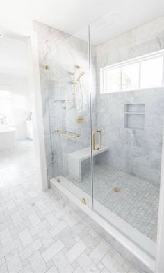a white bathroom with marble tile flooring and gold accents on the shower door, toilet and bathtub