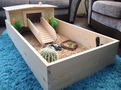 a wooden box filled with plants and rocks on top of a blue rug in front of a couch