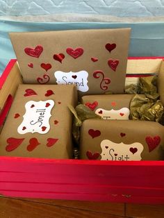 several wrapped presents in a red box with hearts on the sides and tags attached to them