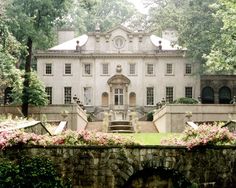 a large house with many windows and flowers in the foreground, surrounded by greenery