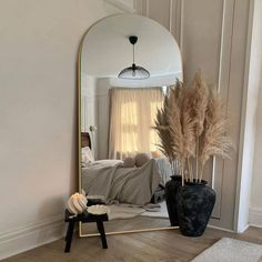 a mirror sitting on top of a wooden floor next to a vase filled with plants