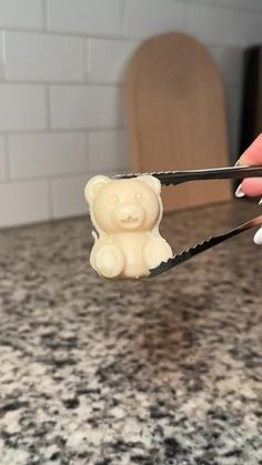 a person holding scissors with a small bear on it's handle in front of a counter top