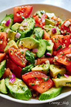 a white bowl filled with cucumber, tomato and avocado salad on top of a table