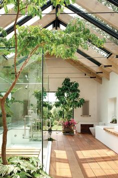 the inside of a house with wood flooring and glass walls on one side, trees in the other