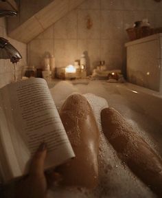a person laying in a bathtub reading a book with water running down the side