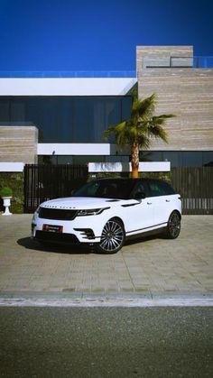 a white range rover parked in front of a modern building with palm trees on the driveway