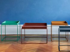 three different colored tables sitting on top of a hard wood floor next to a blue wall