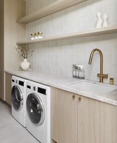 a washer and dryer in a room with white tile flooring, wooden cabinets and shelving