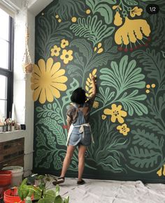 a woman painting a wall with yellow flowers on green and yellow florals in the background