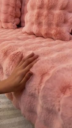 a person reaching for a pink comforter on top of a bed with fluffy pillows