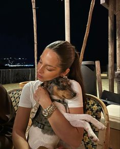 a woman holding a dog in her arms while sitting on a chair outside at night