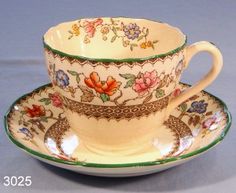an ornate tea cup and saucer with floral designs on the rim, set against a gray background