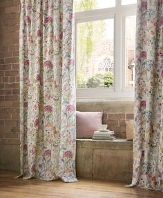 a window with floral curtains and pillows in front of the windowsill, next to a brick bench
