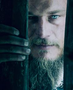 a man with a long beard is looking out from behind the bars in a dark room
