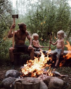 a man and two children sitting around a campfire with an ax in their hands