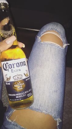 someone is holding a bottle of corona beer in their left hand and ripped jeans on the floor