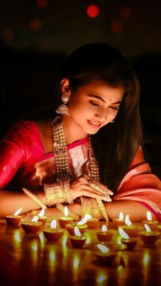 a woman sitting at a table with candles in her hand and looking down on the ground