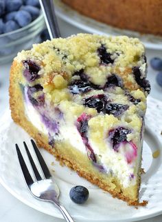 a slice of blueberry cheesecake on a white plate with a fork and bowl of blueberries in the background