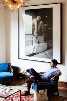 a man sitting in a chair next to a blue couch and a painting on the wall