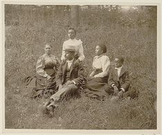 an old black and white photo of people sitting in the grass with one man wearing a hat