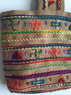 a handbag hanging on the wall with colorful threadwork and letters written in multicolored yarn