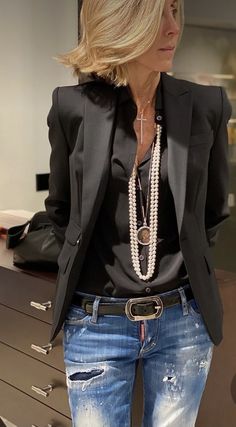 a woman standing in front of a mirror wearing jeans and a black blazer jacket