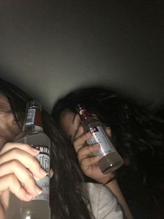 two people are laying down and drinking from water bottles in the dark with their faces close to each other