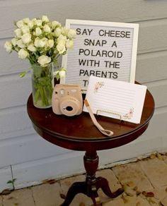 a small table with flowers and a sign on it that says say cheese snap a polaroid with the parents