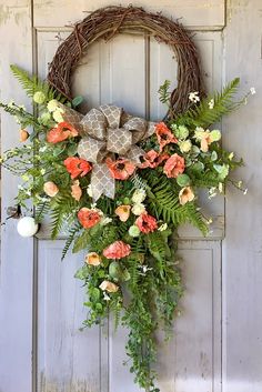 a wreath is hanging on the door with flowers and greenery around it in front of an old wooden door