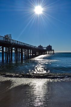 the sun shines brightly over an ocean beach with a pier in the foreground