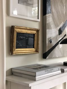 two books are sitting on a shelf in front of some framed pictures and a painting